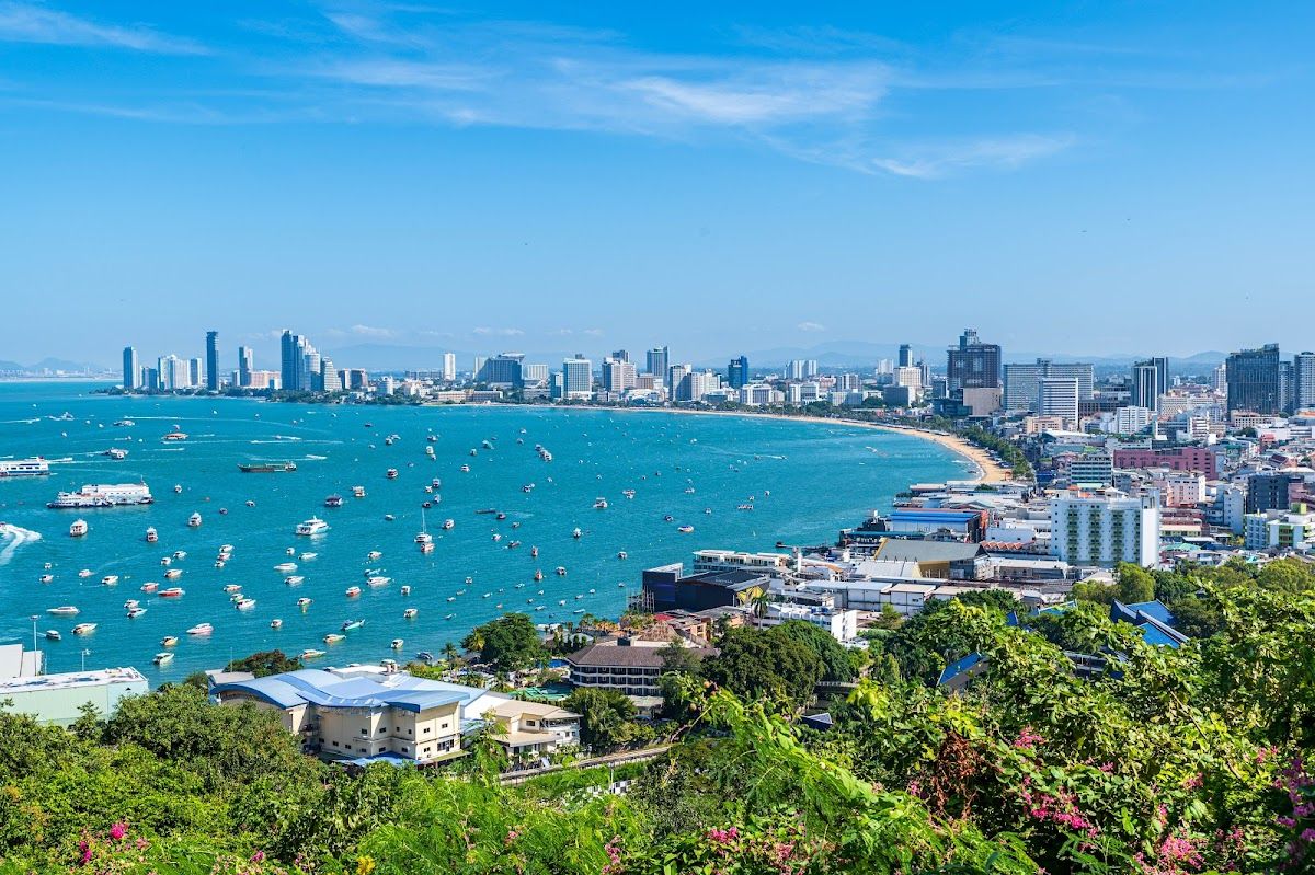 Aerial view of Pattaya Bay from Pratumnak Hill — the curved coastline, boats on the water, and the city skyline under a blue sky