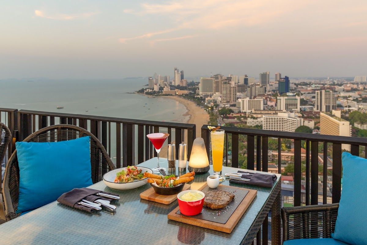 A table for two at Horizon Rooftop Restaurant, Hilton Pattaya, with cocktails and dinner set against a sweeping sunset view of Pattaya Bay and the city skyline