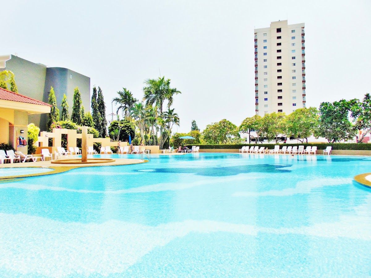 Large outdoor pool at a Jomtien condo complex in Pattaya with sun loungers, palm trees and a high-rise residential tower behind