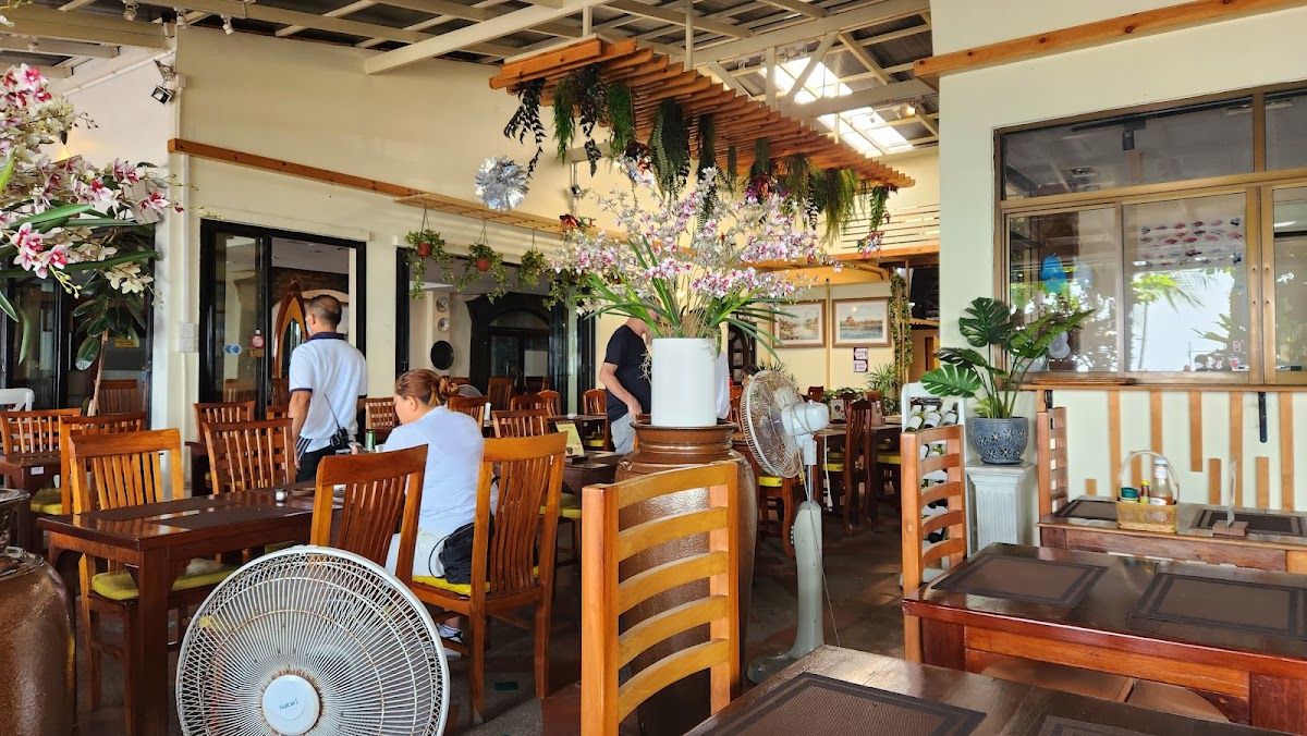 Interior of a relaxed Jomtien beachside restaurant with flowers, wooden furniture, and local diners