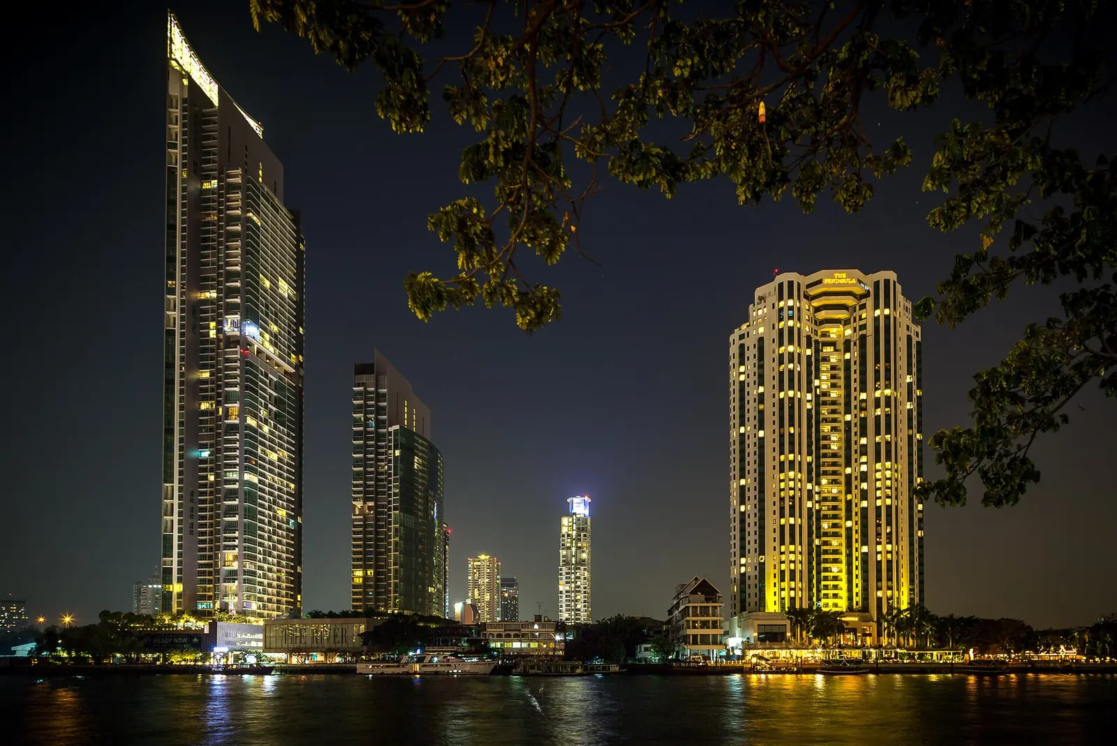 Bangkok at night along the Chao Phraya River, with towers and a lit boat
