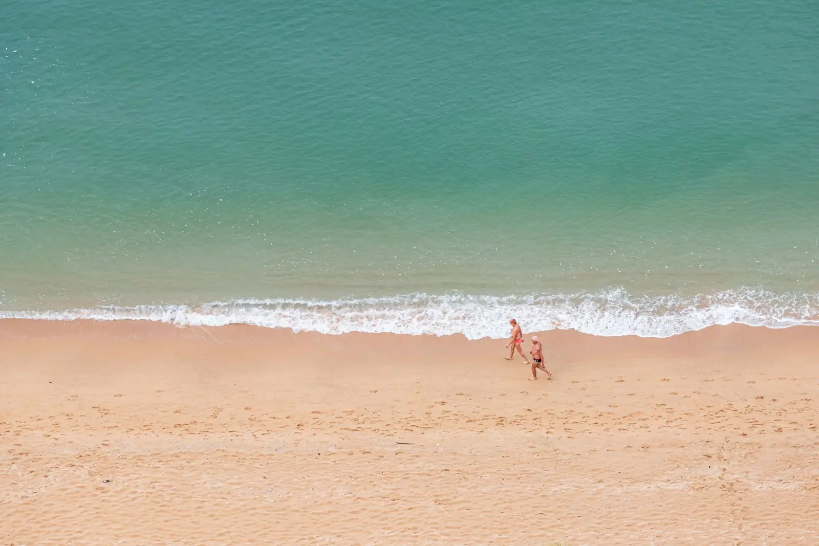 Two people walking on the sand at Pattaya Beach with the sea beside them