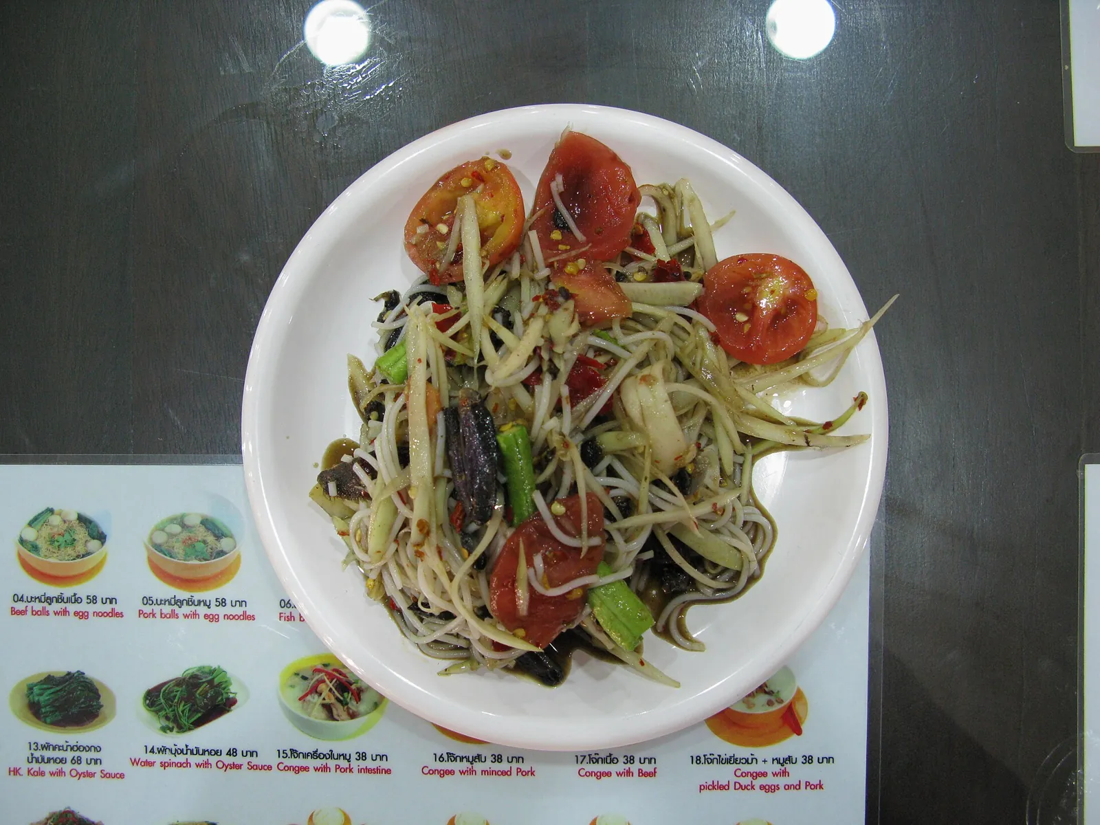 A plate of green papaya salad with lime, tomato and long beans
