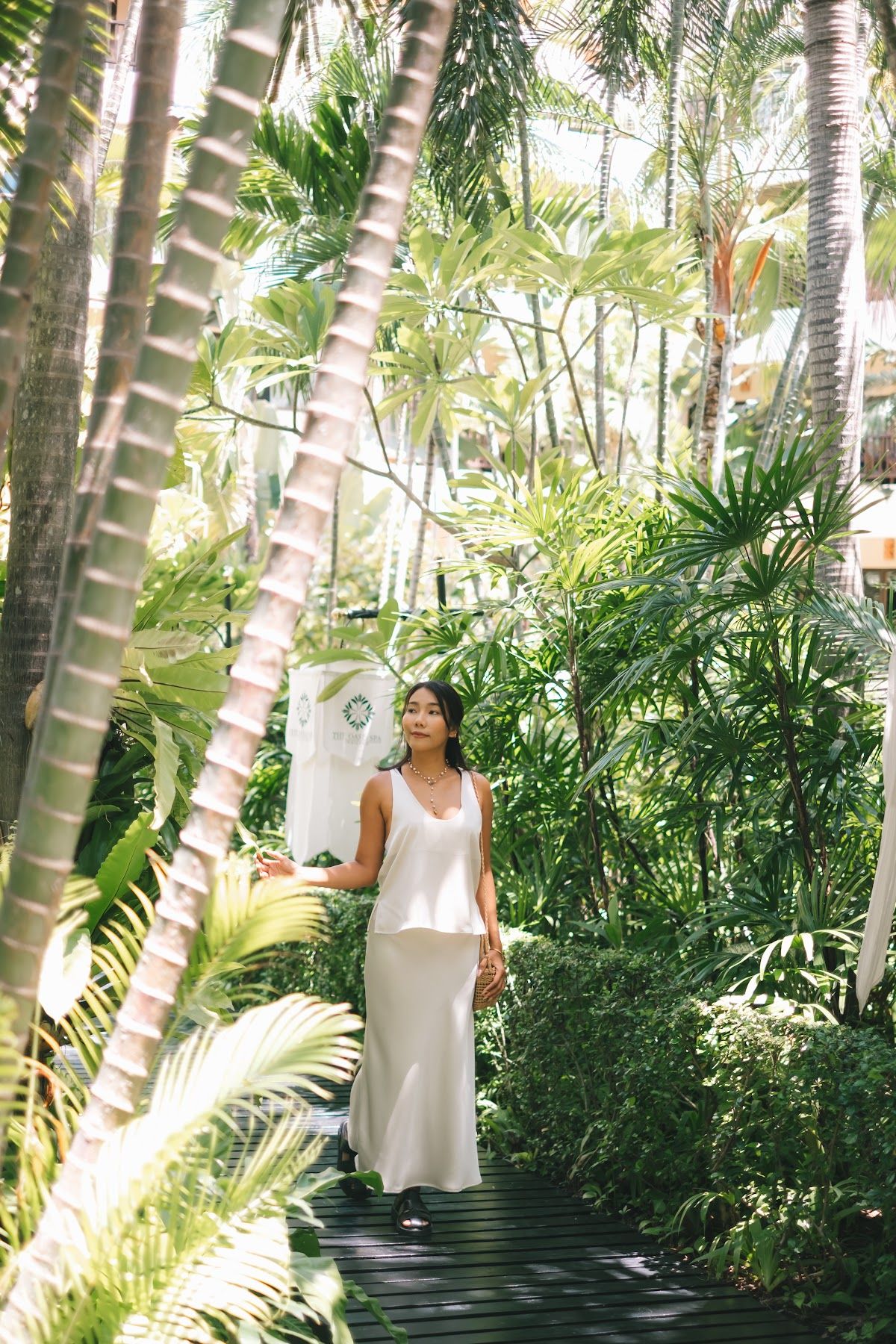 The garden path through Oasis Spa Jomtien, lined with tall palms and dense tropical greenery under dappled light