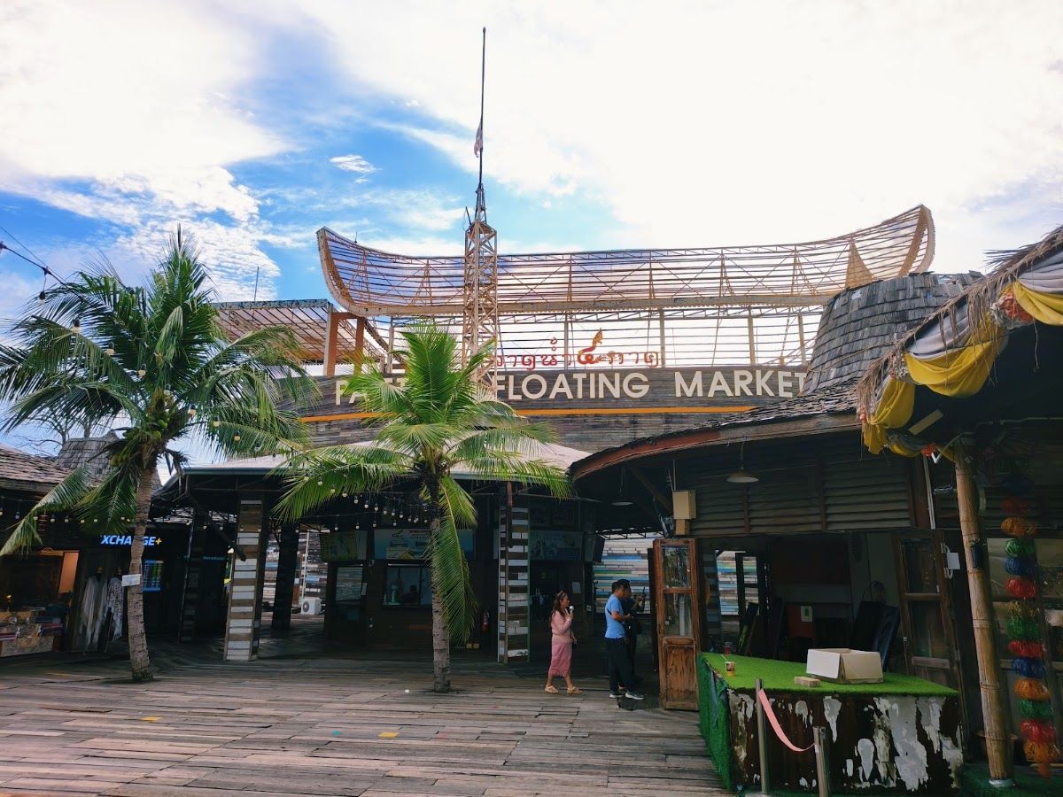 Pattaya Floating Market entrance on a sunny day with palm trees and a wooden boardwalk leading to traditional Thai roof architecture
