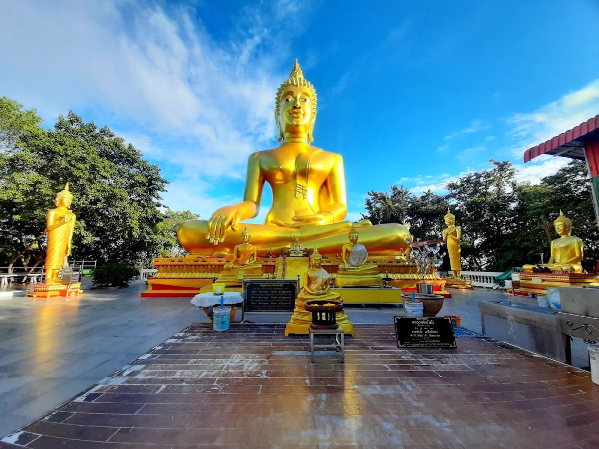 The 18-metre golden Buddha statue at Wat Phra Yai on Pratumnak Hill, Pattaya, with smaller golden Buddha statues and tropical trees under a blue sky